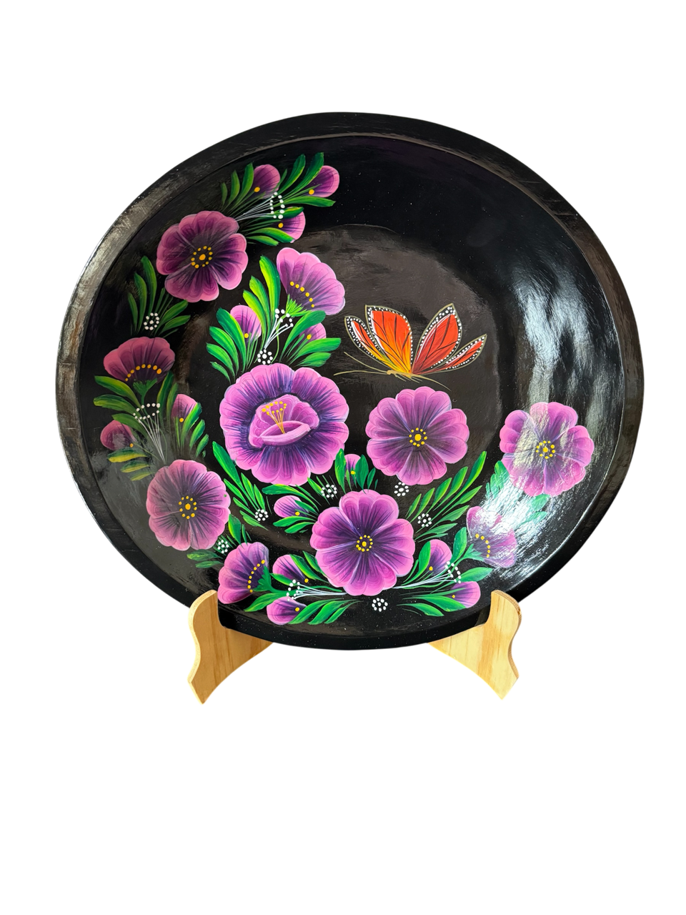 Vista frontal completa de una batea redonda de madera negra con diseño central de mariposa monarca y flores moradas, una obra de arte popular purépecha de Mansión Iturbe Artisans Collection.