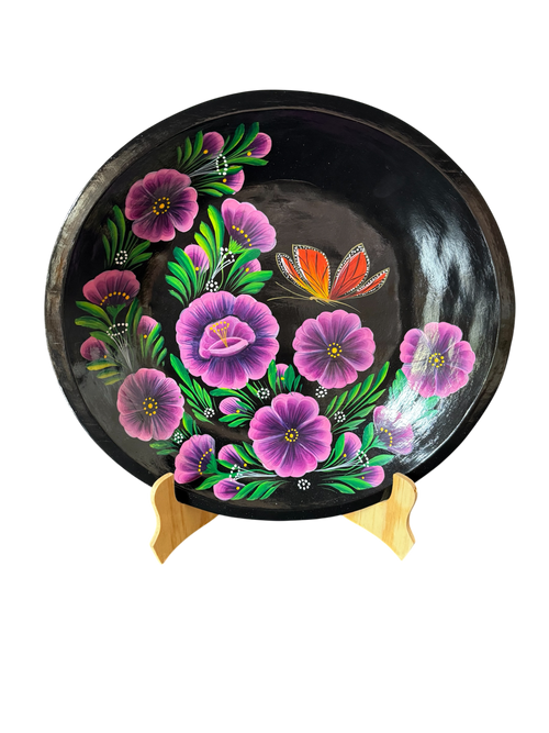Vista frontal completa de una batea redonda de madera negra con diseño central de mariposa monarca y flores moradas, una obra de arte popular purépecha de Mansión Iturbe Artisans Collection.