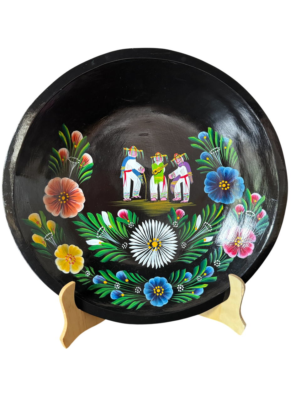 Vista frontal completa de una batea circular de madera negra pintada a mano con la Danza de los Viejitos al centro y flores tradicionales en tonos azul, blanco, amarillo y rosa alrededor.