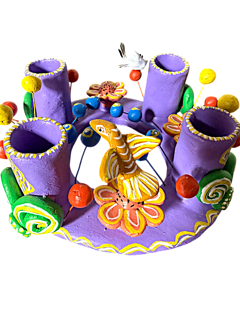 Fotografía en perspectiva de tres cuartos de un candelabro de barro policromado de Ocumicho. Se aprecia el volumen de las figuras de pajaritos y flores artesanales modeladas a mano sobre la base circular plana de color lila.