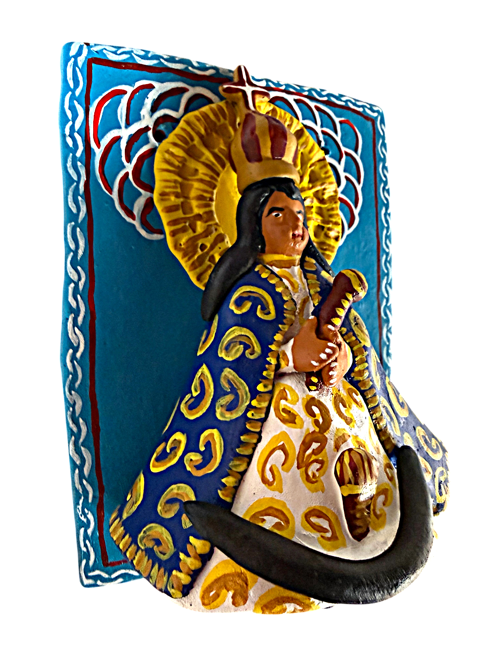 Primer plano en ángulo de la escultura de la Virgen en alto relieve sobre el retablo azul. Se aprecia la textura del barro modelado a mano y la pintura detallada de los diablitos y las flores que la rodean. Pieza única de Mansión Iturbe Artisans Collection.